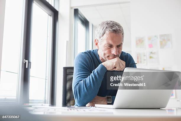 mature man sitting in office using laptop - laptop stock-fotos und bilder