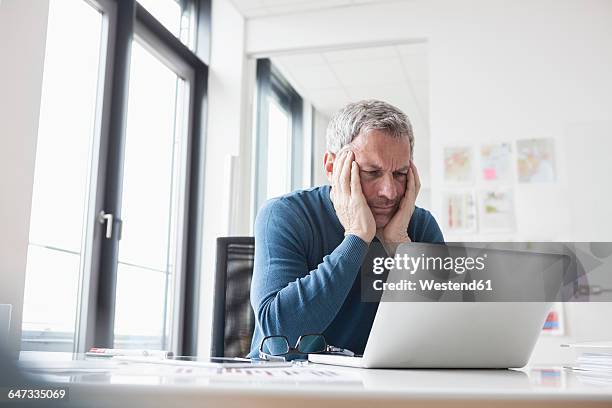 mature man sitting in office using laptop - frustration man stock pictures, royalty-free photos & images