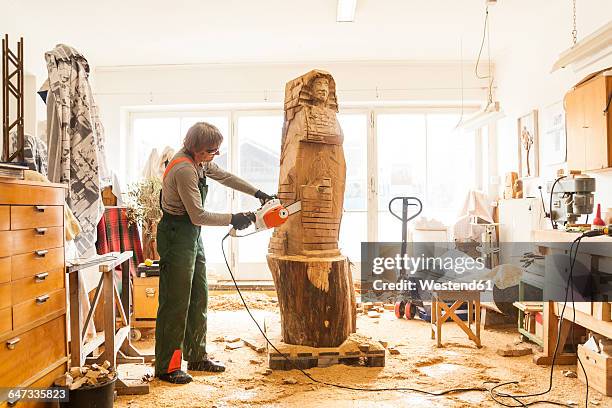 wood carver in workshop working on sculpture with chainsaw - scultura fotografías e imágenes de stock