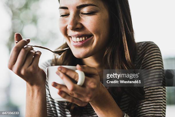 young woman drinking cappuccino, spooning milk froth - indulgence stockfoto's en -beelden