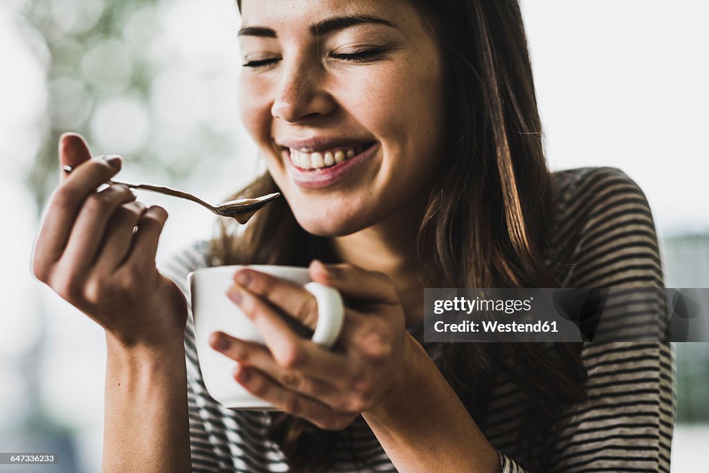 Young woman drinking cappuccino, spooning milk froth