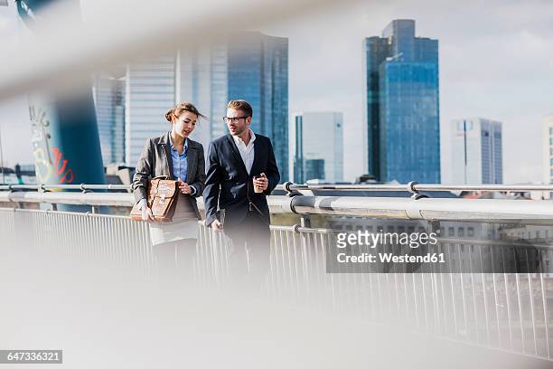 young business couple walking on bridge, talking - wolkenkratzer stock-fotos und bilder