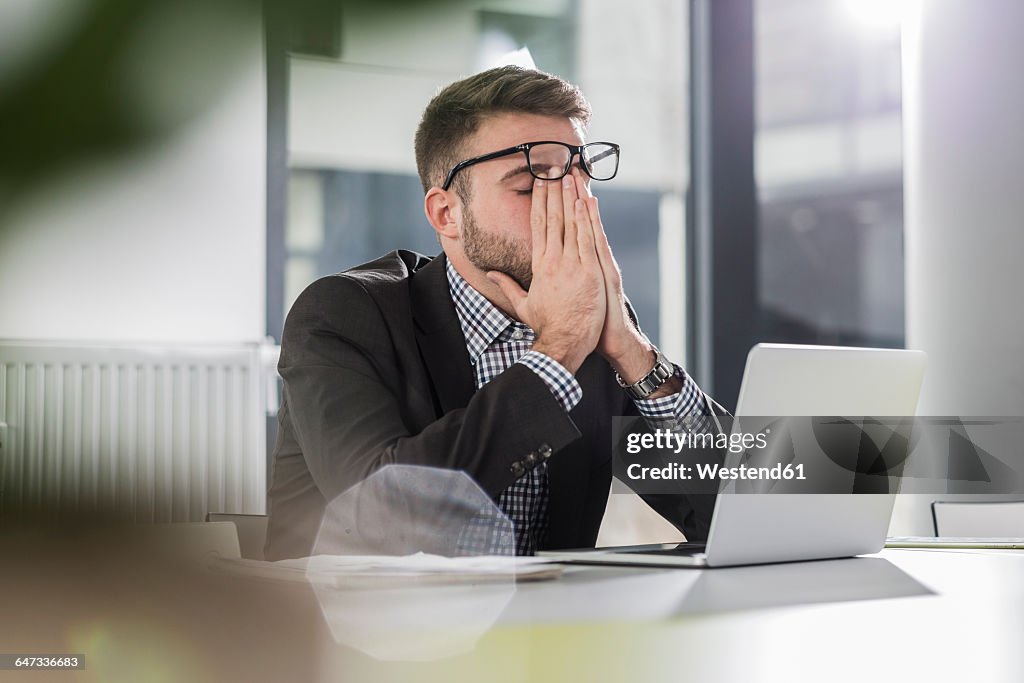 Exhausted young man with laptop in office