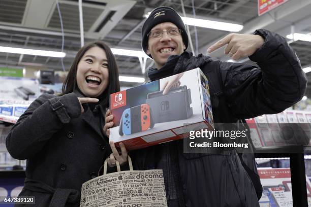 Customers pose with a box of Nintendo Co. Switch game console in this arranged photograph after they purchased the hybrid console at a Bic Camera...