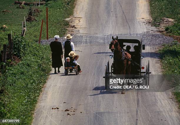 Amish families passing on the road, one on foot and the other on horse-drawn carriage, Lancaster, Pennsylvania, United States of America.