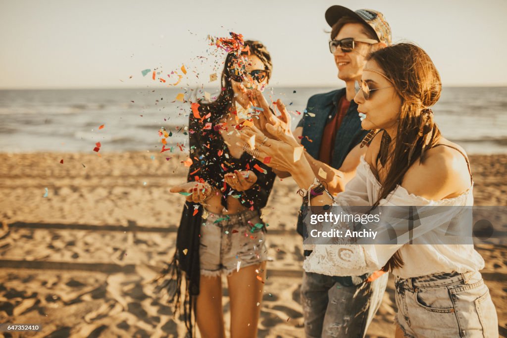Happy vrienden feesten op het strand met drankjes en confetti. Gelukkige jonge mensen plezier op strand feest vieren met confetti.