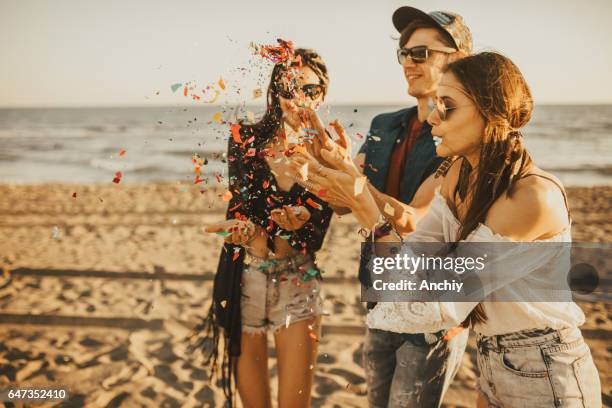 happy friends partying on the beach with drinks and confetti. happy young people having fun at beach party, celebrating with confetti. - sky crackers stock pictures, royalty-free photos & images