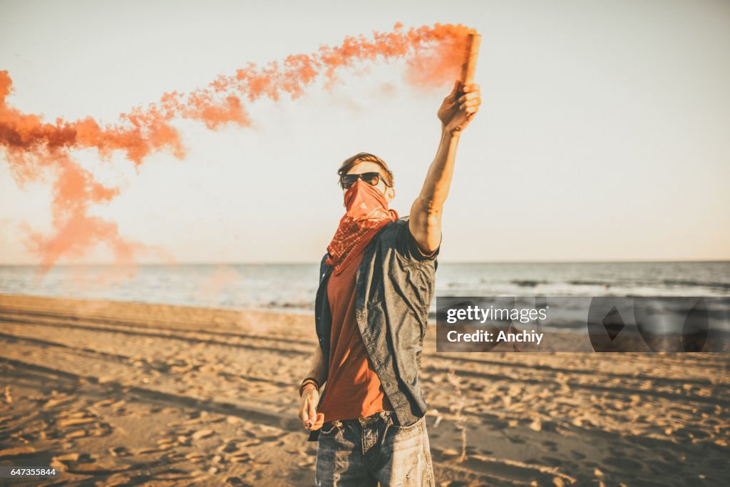 Riot Hipster Man holding red smoke on the beach