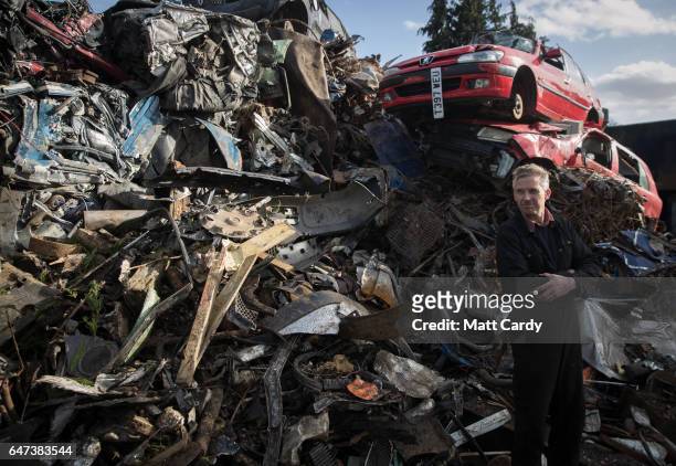 Yard owner Ped Rossiter poses for a photograph in front of a pile of scrap metal and scrap cars waiting to be processed at Pylle Motor Spares and...
