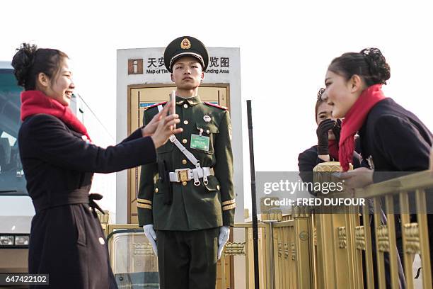 Hostesses take pictures next to a paramilitary guard during the opening session of the Chinese People's Political Consultative Conference in the...
