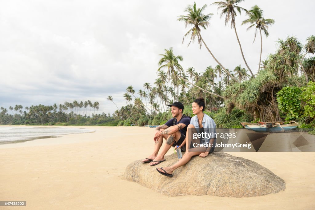 Mid adult couple sitting on rock on beach