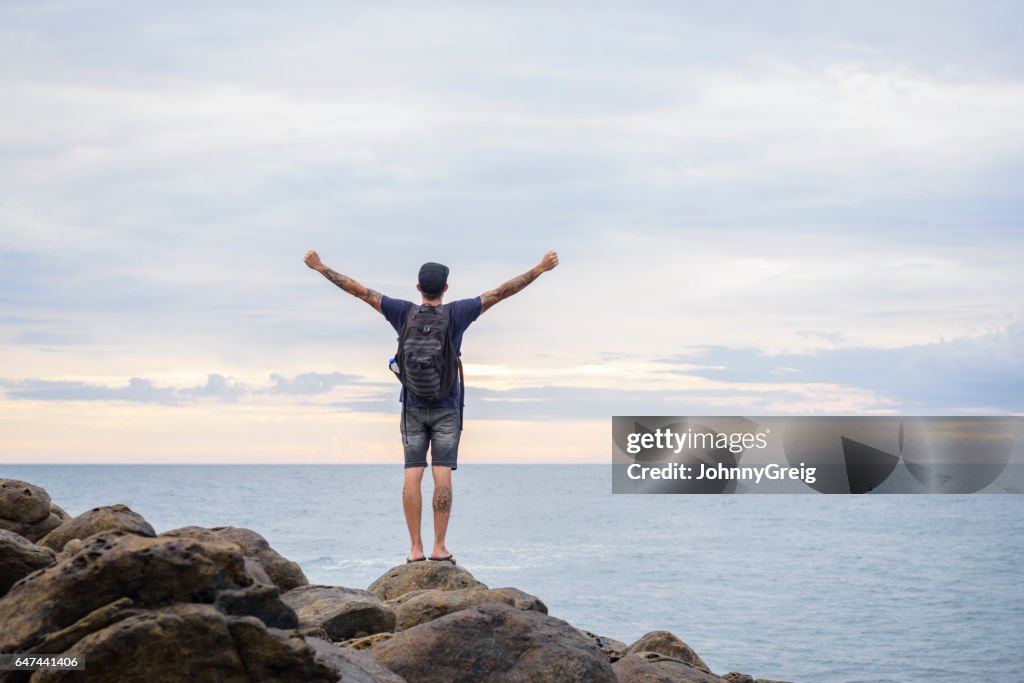 Male backpacker standing on rocks with arms outstretched