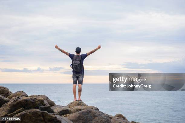 male backpacker standing on rocks with arms outstretched - gap year stock pictures, royalty-free photos & images