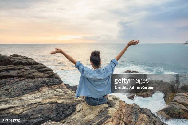 rear view of woman on coastline with arms outstretched - top garment stock pictures, royalty-free photos & images