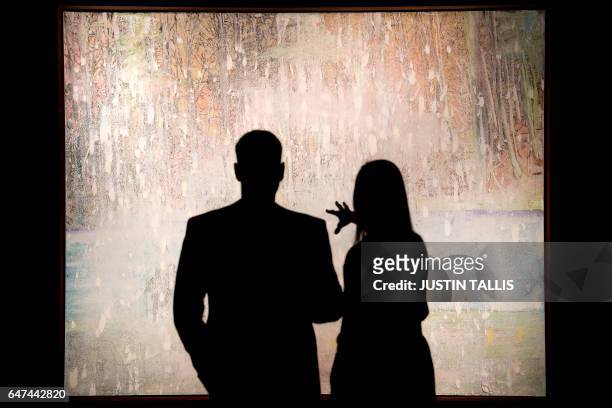 Visitors are seen with an artwork by British artist Peter Doig entitled "Cobourg 3 + 1 More", with an estimated price of 8-12 million GBP during a...