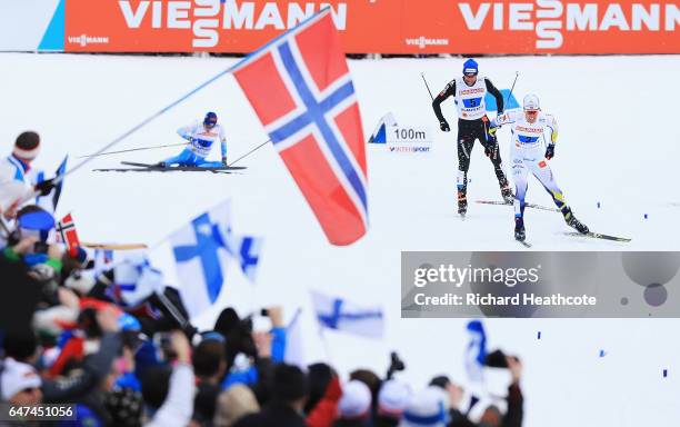 Calle Halfvarsson of Sweden and Curdin Perl of Switzerland head for the finish line as Matti Heikkinen of Finland crashes in the Men's 4x10km Cross...