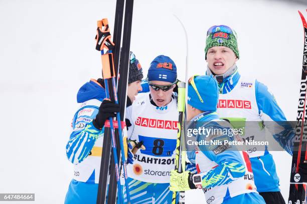 Matti Heikkinen of Finland is comforted by team-mates after falling in the last curve during the men's cross country relay during the FIS Nordic...