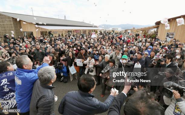 Business owners throw rice cakes to celebrate the opening of their stores on March 3 at a new commercial facility in Minamisanriku, Miyagi...