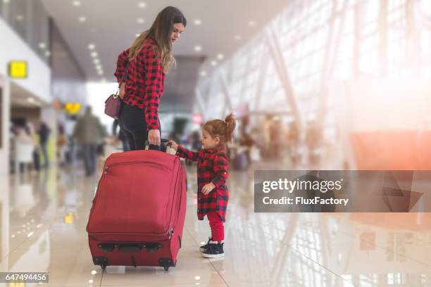 mother and cute toddler girl pulling together a suitcase - airport sitting family stock pictures, royalty-free photos & images