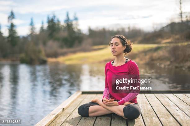 joven mamá haciendo yoga fuera por lago - good posture fotografías e imágenes de stock