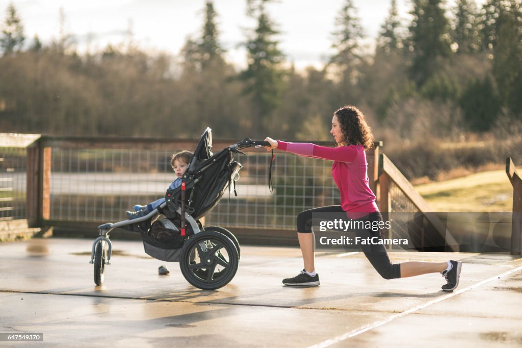 Young mom stretching next to child in baby stroller