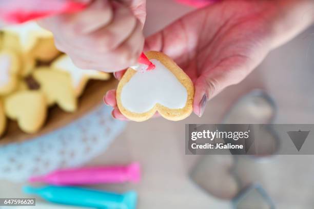 overhead view of a woman icing a heart shaped cookie - homemade valentine stock pictures, royalty-free photos & images