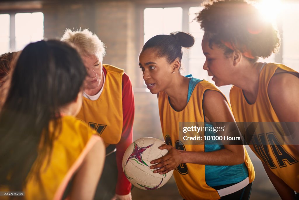 Female netball team talking in gym.