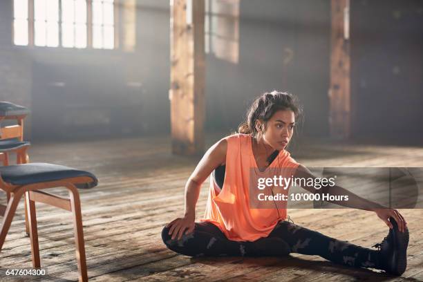 young woman with earbuds stretching in gym. - woman sportswear stock pictures, royalty-free photos & images