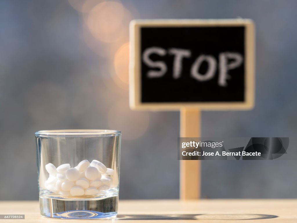 Glass of crystal with an overdose of medicines i a sign with the stop sign , illuminated by the light of the Sun