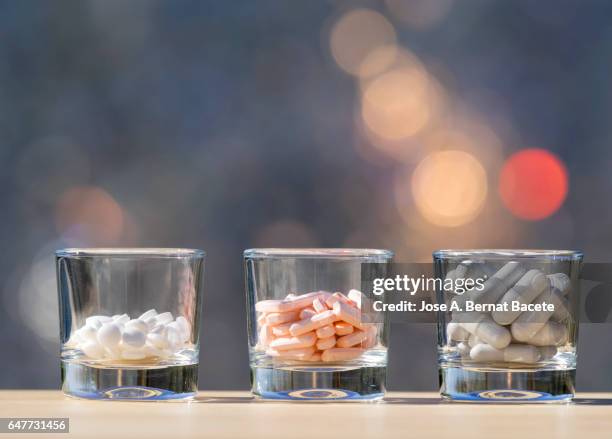 three glass glasses with dangerous overdose of different medicines , illuminated by the light of the sun - doping pills stock pictures, royalty-free photos & images