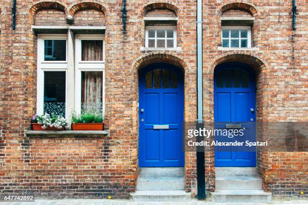 two identical doors and a window in a red brick house - blue house red door stock pictures, royalty-free photos & images