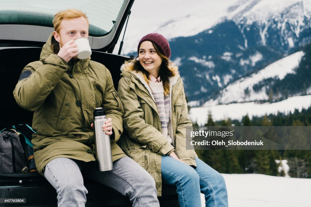 Friends resting and drinking hot drink near the car in mountains