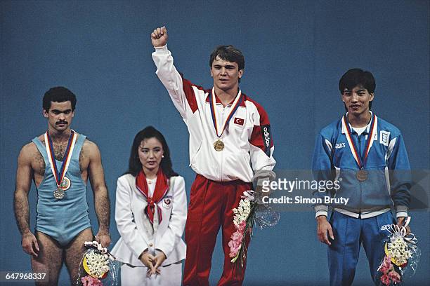 Naim Suleymanoglu of Turkey celebrates his gold medal on the podium alongside silver medallist Stefan Topurov of Bulgaria and bronze medallist Ye...
