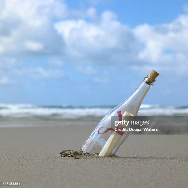 glass bottle in sand at beach with message inside. - message in a bottle stock pictures, royalty-free photos & images