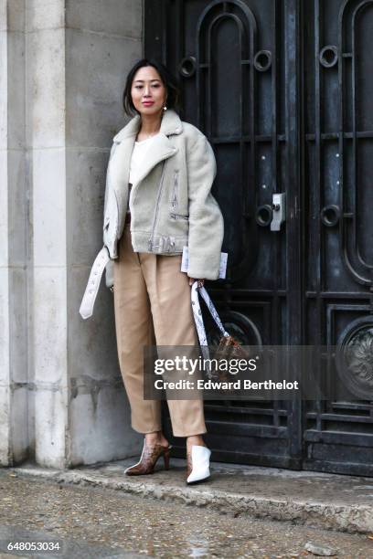 Aimee Song, fashion blogger from Song of Style, wears a white fur aviator jacket, a white top, beige pants, bicolor white and snake print shoes, and...