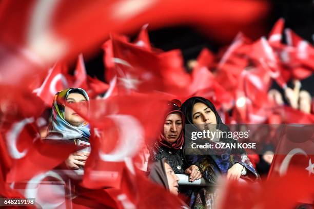 Women look on as they are surrounded by supporters waving Turkish national flags on March 5, 2017 in Istanbul during a pro-government women meeting....