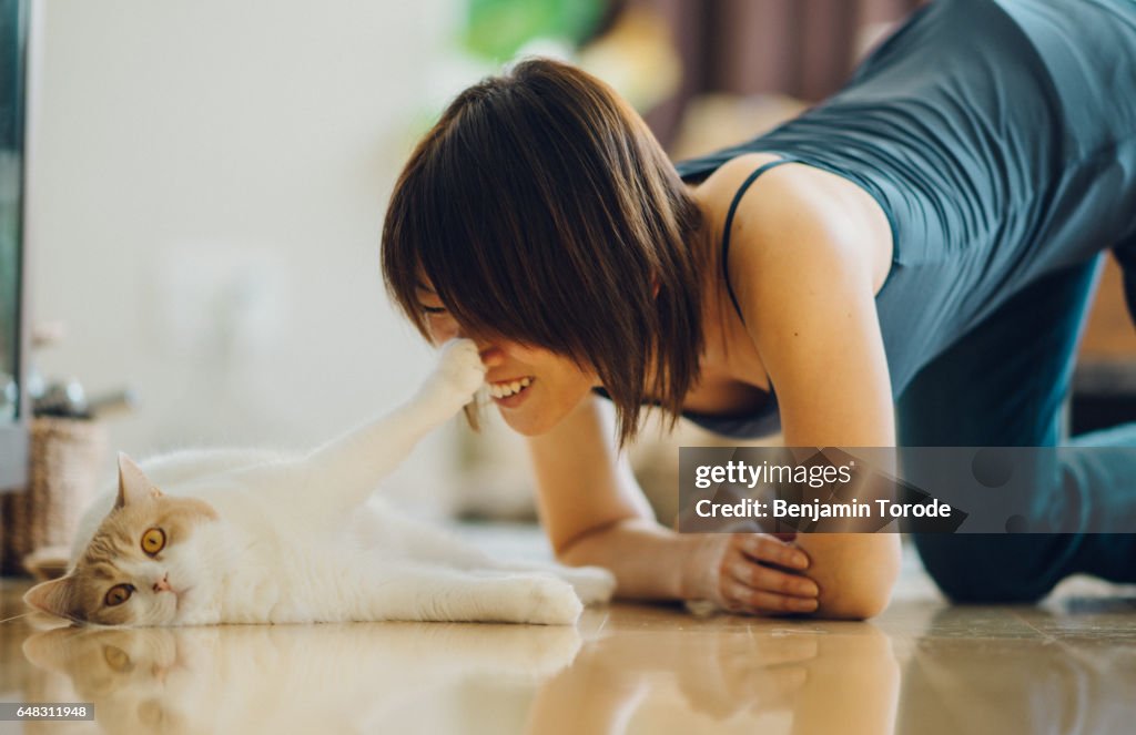 Beige and white cat looks at camera as it pushes on face of smiling Japanese girl with paw