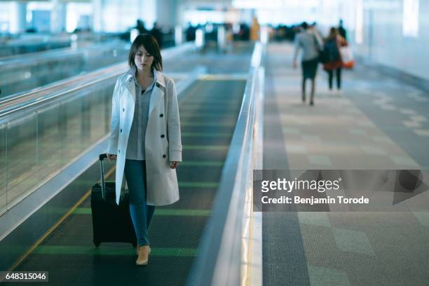 japanese woman on moving walkway in airport terminal pulling luggage - travolator stock pictures, royalty-free photos & images