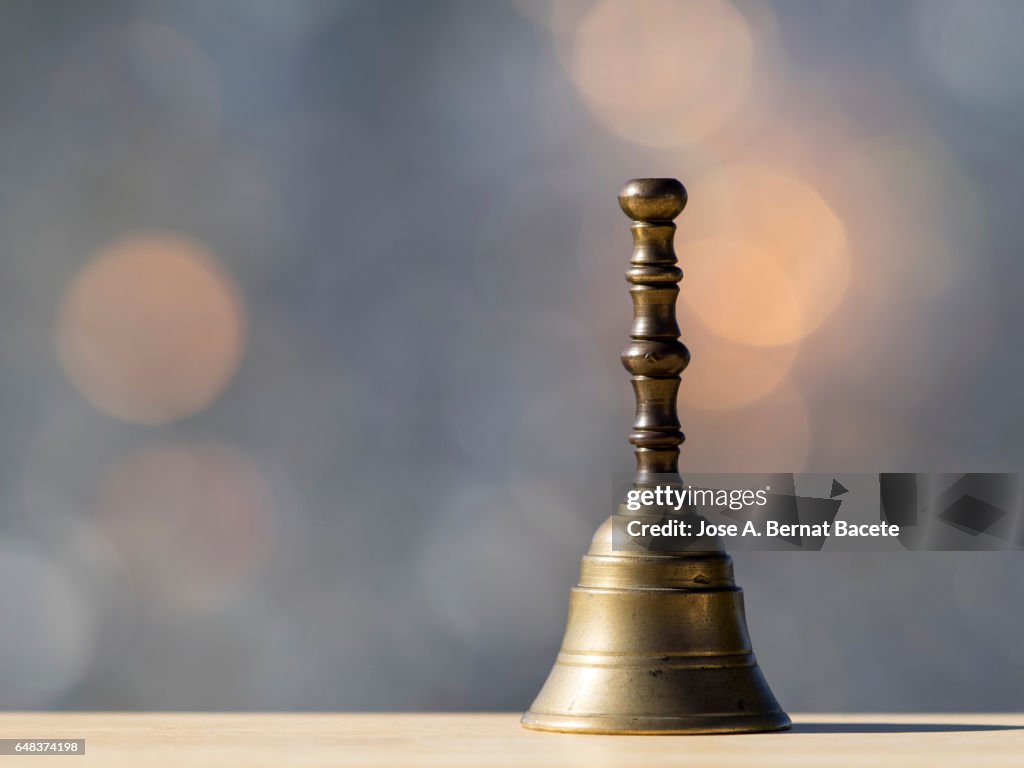 Hand small bell of metallic hand, on a table of wood illuminated by the light of the Sun