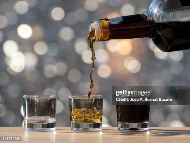 glass of crystal of chupito fill of an alcoholic drink, filling them with a bottle of drink  , illuminated by the light of the sun - cirrhosis 個照片及圖片檔