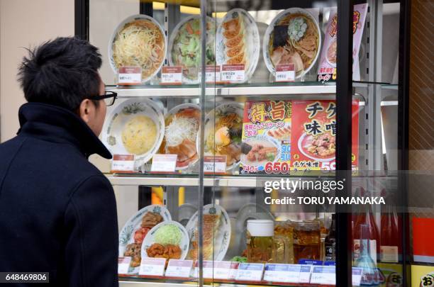 This photo taken on January 19, 2017 shows a customer looking at a display of fake food dishes at the window of a Chinese restaurant in Tokyo. They...