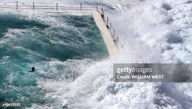 Swimmer at Bondi's ocean pool watches as a big wave pours into the pool as large seas pound the coast at Bondi Beach in Sydney on March 6, 2017.