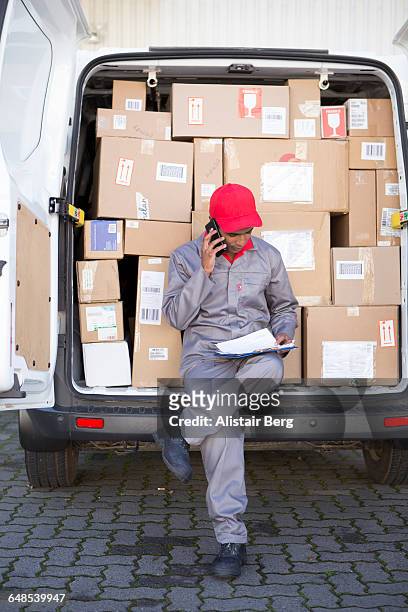 courier delivering parcels and boxes - guy with phone full image ストックフォトと画像