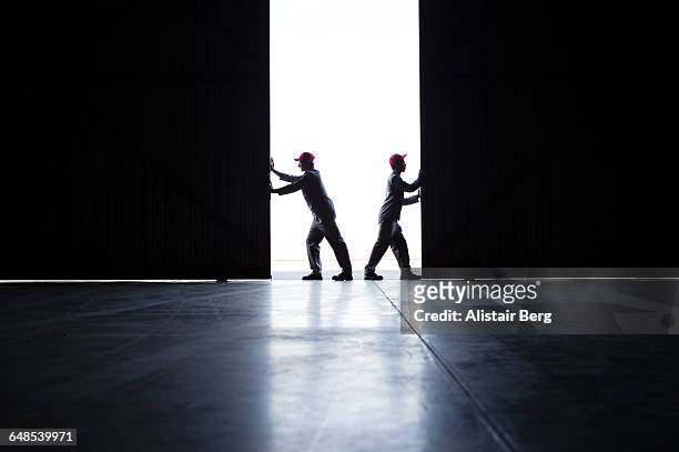 two men pushing open doors - hangar stockfoto's en -beelden