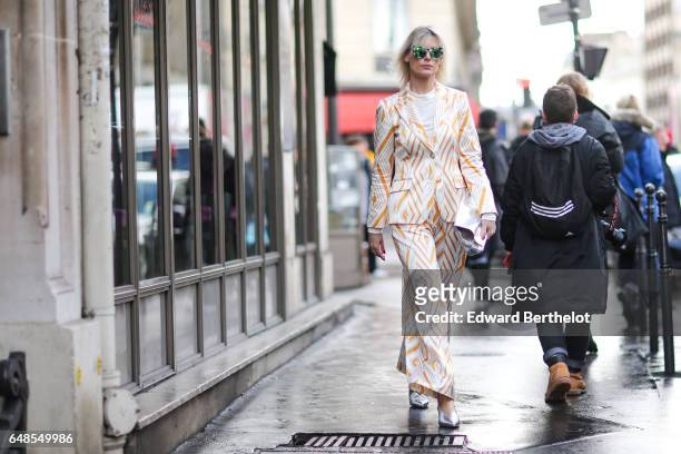 Guest wears green sunglasses, a white top, a white and orange striped suit, and silver shoes, outside the Valentino show, during Paris Fashion Week...