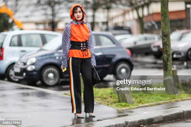 Fashion blogger Miu wears an orange hoodie sweater with blue and white checked sleves and collar, a black large belt, and black sportswear pants with...