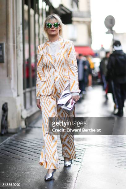 Guest wears green sunglasses, a white top, a white and orange striped suit, and silver shoes, outside the Valentino show, during Paris Fashion Week...