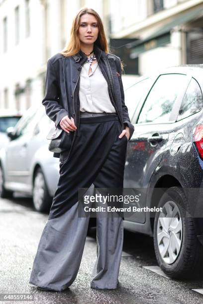 Guest wears a gray jacket, a white shirt, a black silk skirt, and gray flared silk pants, outside the Valentino show, during Paris Fashion Week...