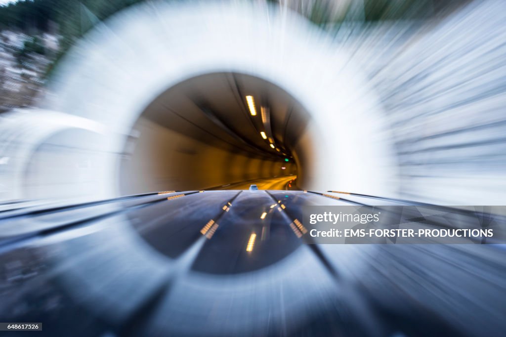 Automotive on board a car long exposure rigging shot of the top of a black german van, streaking reflections in the roofs surface of the car in foreground, antenna and front end of the roof in mid ground, the background is motion blurred.