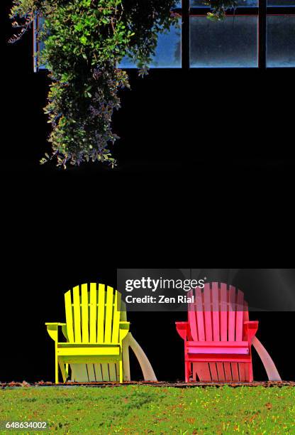 front view of two adirondack pink and yellow colored chairs and tree branch on black background - liegestuhl freisteller stock-fotos und bilder